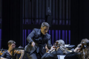 man in black suit, conducts orchestra