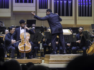 Conductor leads orchestra with cello soloist in the foreground