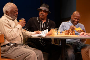 Three men at table, eating, playing chess